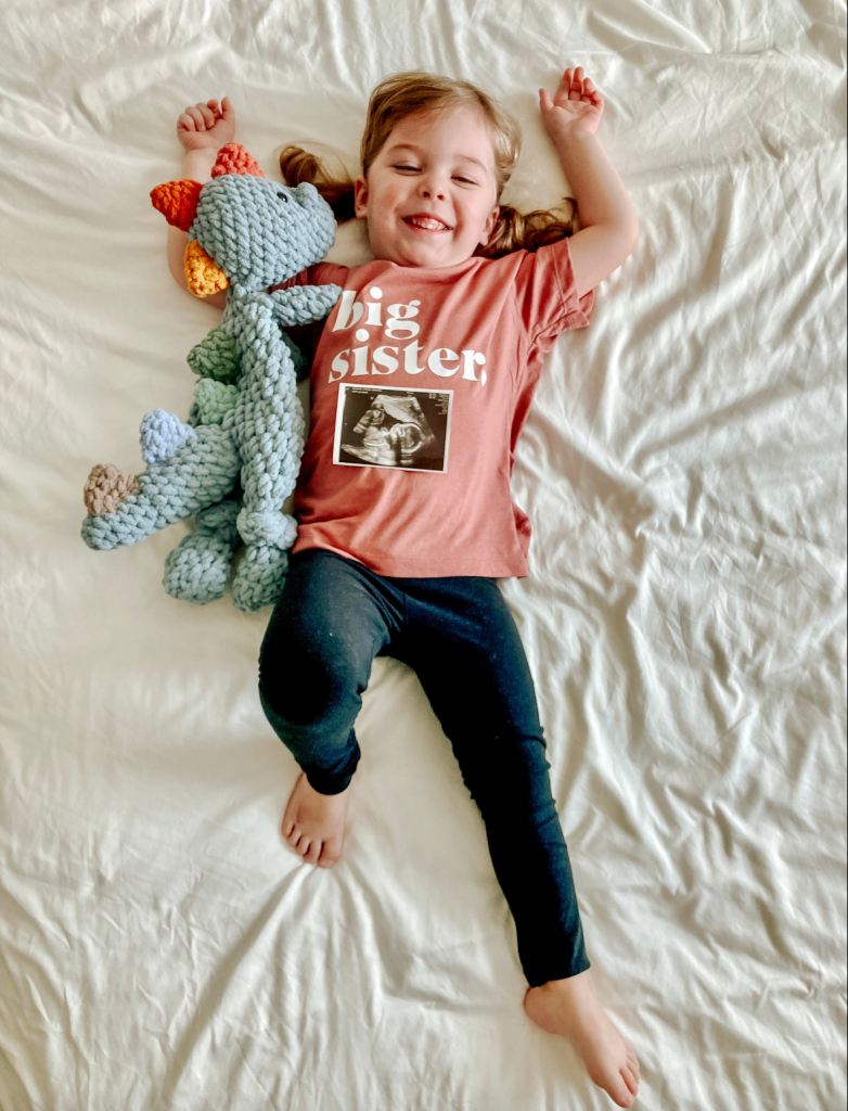 Idee voor zwangerschapsaankondiging: kind met shirt aan "big sister" en echofoto vast met snuggler.