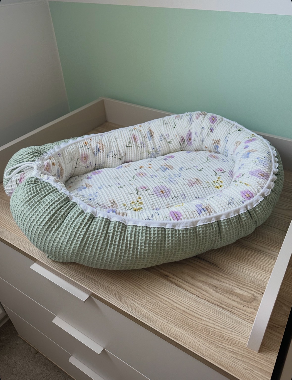Dit handgemaakte babynestje van wafelkatoen in zacht groen en gebroken wit met lenteprint geeft je baby een comfortabele en geborgen plek om te rusten.
